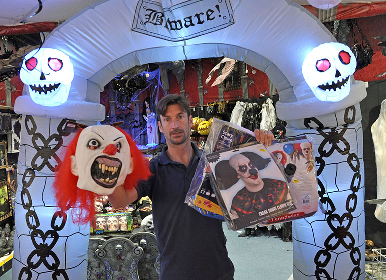 Nick Peeks with clown costumes in front of one of the giant party store’s Halloween displays